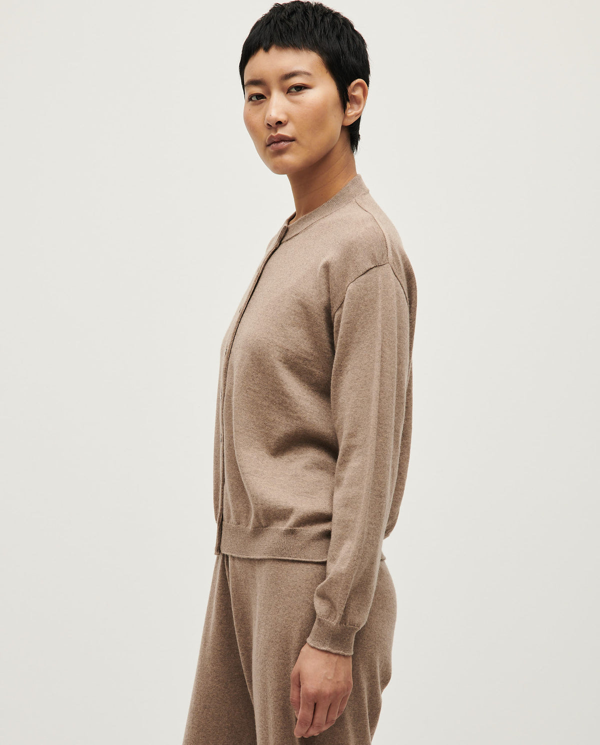 White Babaà No25 women's cardigan draped on a hanger, showcasing its soft knit texture and relaxed fit.